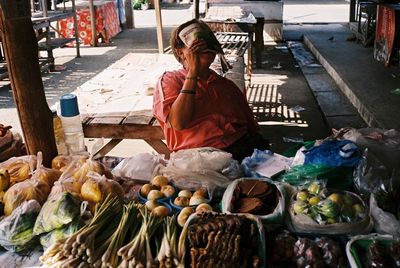 Happy woman covering face with magazine while sitting at market stall