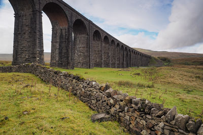 Arch bridge on field against sky