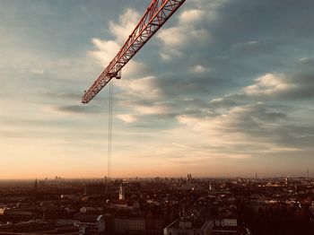 Crane in city against sky during sunset