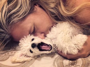 Close-up of mature woman pampering dog on bed 