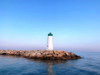 Lighthouse on rock by sea against clear sky