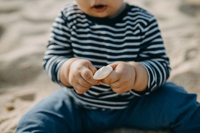Midsection of cute boy playing with sea shell on beach