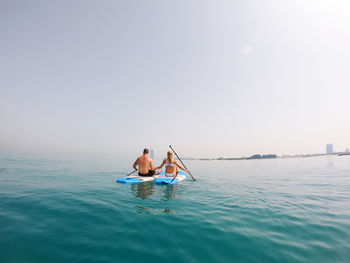 People on paddle board in sea against sky