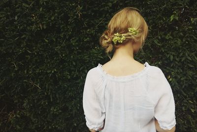 Rear view of woman with flowers in hair while standing against plants