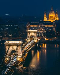 Illuminated bridge over river in city at night