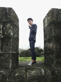 Young man standing on rock against sky