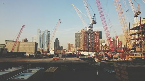 Low angle view of cranes and buildings in city against sky