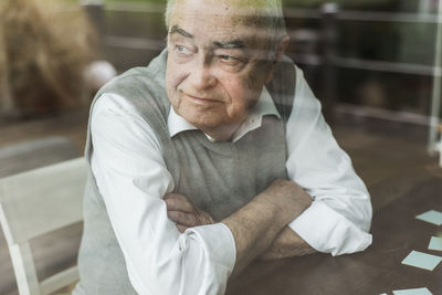 Portrait of senior man with crossed arms looking through window