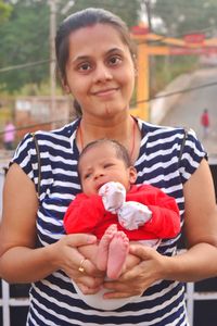 Portrait of mother carrying baby boy while standing outdoors