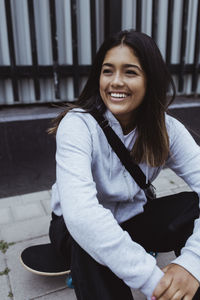 Smiling teenage girl sitting on skateboard at footpath