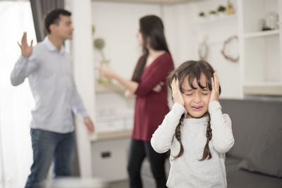 Close-up of girl crying while parents fighting in background at home