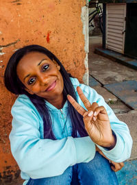 Portrait of smiling young woman showing peace sign