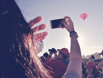 Midsection of woman photographing with mobile phone against sky