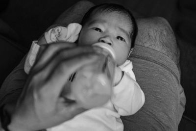 Midsection of man feeding milk to baby boy on lap at home