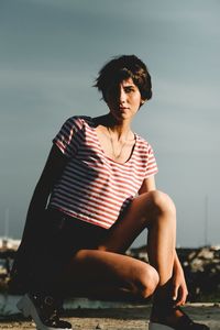 Portrait of young woman crouching on street against sky during sunset