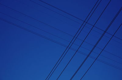 Low angle view of power lines against clear blue sky