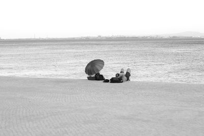 People sitting on shore by sea against clear sky