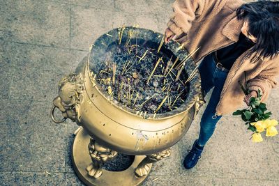 High angle view of girl holding yellow roses while standing by incense in pot at temple