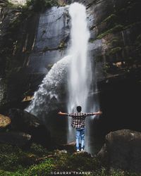 Rear view of man standing by waterfall