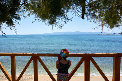 Rear view of boy standing on railing against sea