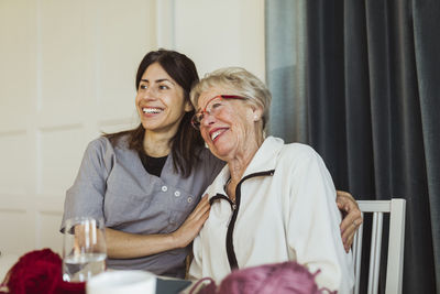 Happy female healthcare worker sitting with senior woman in nursing home