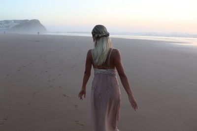 Rear view of woman standing at beach against sky