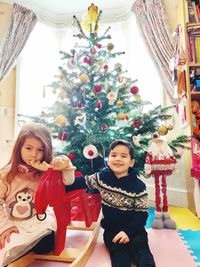 Portrait of siblings against christmas tree at home