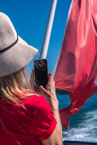 Blonde woman in white cap and red t-shirt taking a photo with the smartphone to the swiss flag.