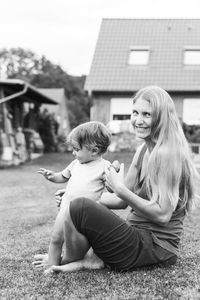 Mother and daughter sitting on house against sky