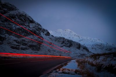 Light trails on road leading towards snowcapped mountains at dusk