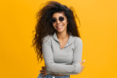 Portrait of young woman standing against yellow background