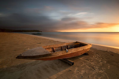 Wooden boat moored at beach against sky during sunset