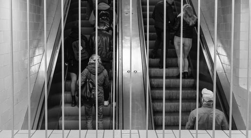 Rear view of people standing on escalator seen through fence at subway station