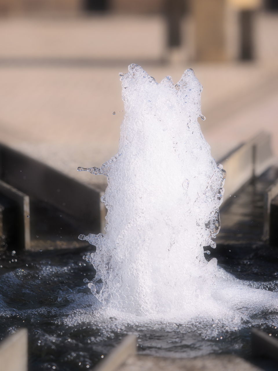 focus on foreground, water, close-up, motion, splashing, selective focus, wet, drop, day, outdoors, fountain, built structure, building exterior, part of, incidental people, architecture, winter, nature