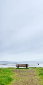 Bench on field by sea against sky