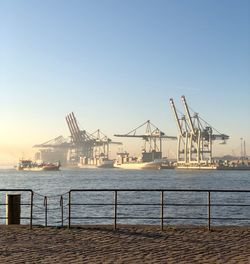 Cranes at harbor against clear sky