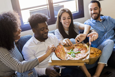 Happy friends sitting on the sofa sharing a pizza