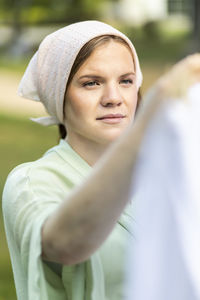 Portrait of young pretty white woman hanging up laundry on clothes line outside, drying bed linens