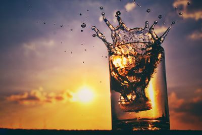 Close-up of water splashing in glass against sunset sky