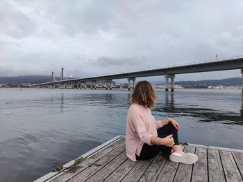 Rear view of woman sitting on bridge against sky