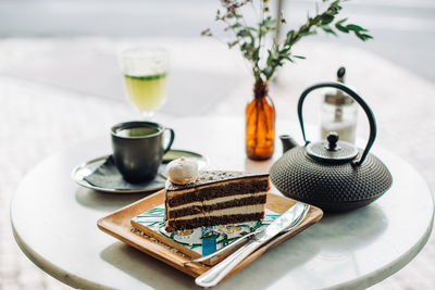 Slice of chocolate cake, teapot, cup of tea on table in outdoors cafe