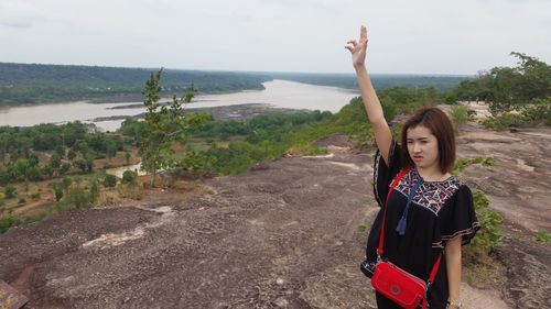 Young woman standing with hand raised on mountain