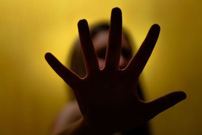 Close-up of woman hand standing against yellow background
