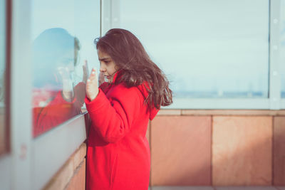 Young woman standing against red wall