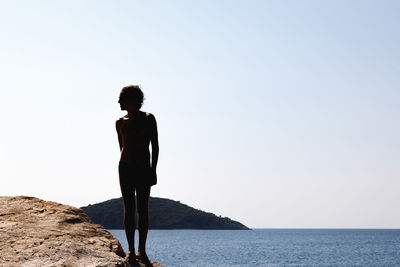 Man standing on rock looking at sea against clear sky