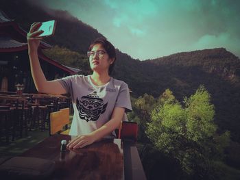 Woman taking selfie through mobile phone against mountains