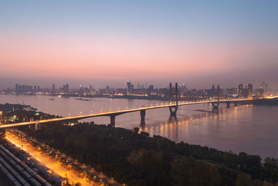 Illuminated bridge over river against sky at sunset