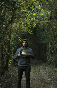 Portrait of man holding mirror while standing in forest