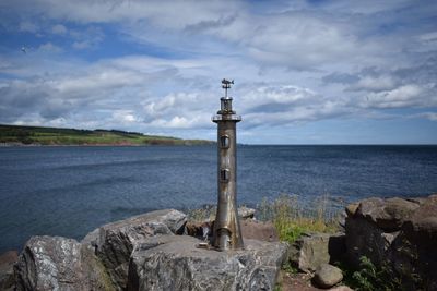 Lighthouse on rocks by sea against sky