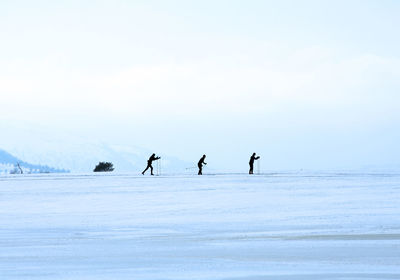 Silhouette people skiing on snow covered field against clear sky